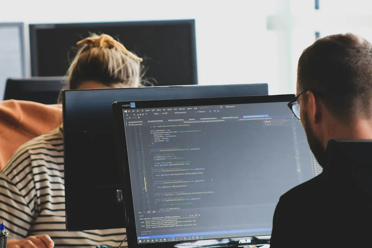 Software developers reviewing code on large monitors in an office
