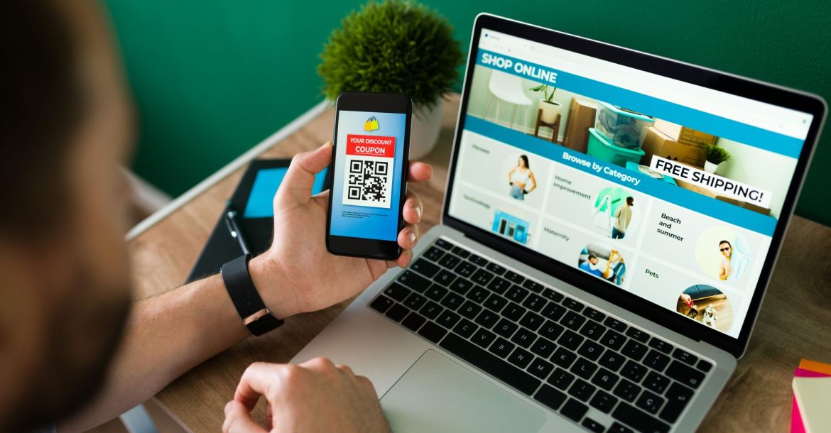 young-man-using-discount-coupon-his-smartphone-some-online-shopping-laptop